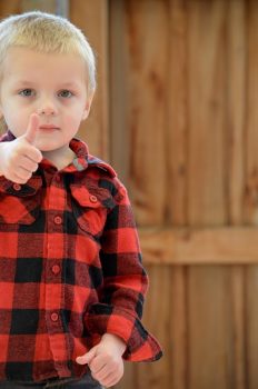 A blond little boy giving a thumbs up to the camera