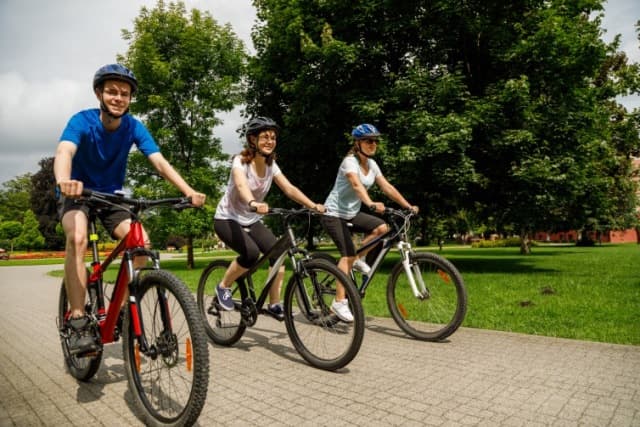 A family bikes together safely through a park.