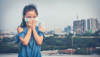 A girl stands outside and holds a mask to her nose