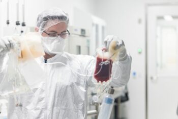 A person in isolation gear looks at bag of blood