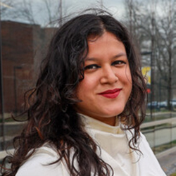 A close up photo of a woman with dark curly hair wearing a cream colored blouse smiling at the camera 