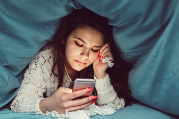 A kid looks at their phone under the bed covers.