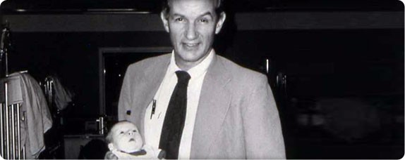 A black and white photo of a man holding a baby while smiling at the camera