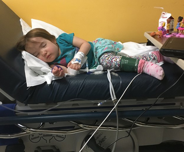 A little girls sleeping on a hospital bed in front of a bright yellow wall