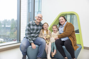 A family smiles at the camera while sitting in a lobby at Seattle Children's Hosptail