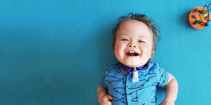 a boy smiles at the camera while laying on a teal yoga mat