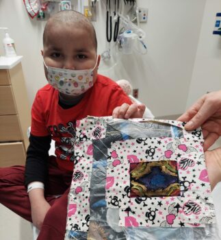 A little boy holds up the piece of fabric he painted that will be quilted onto the spacesuit