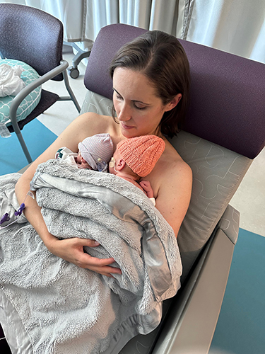 A mother looking down at her two twin newborns who are resting on her chest