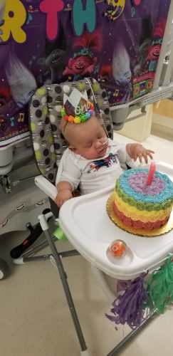 A baby in a high chair with a birthday cake