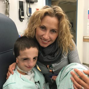 a mom cuddles her son as he sits in a hospital chair in a green striped hospital gown