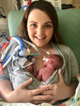 a mother smiles as she shares skin to skin time with her twins in the NICU