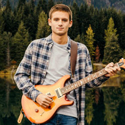 A teen boy stands in front of a forest lake