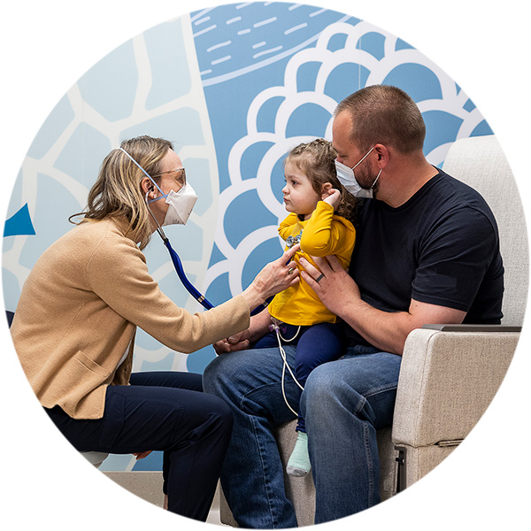 A father holds his daughter as she is examined by a Seattle Children's provider