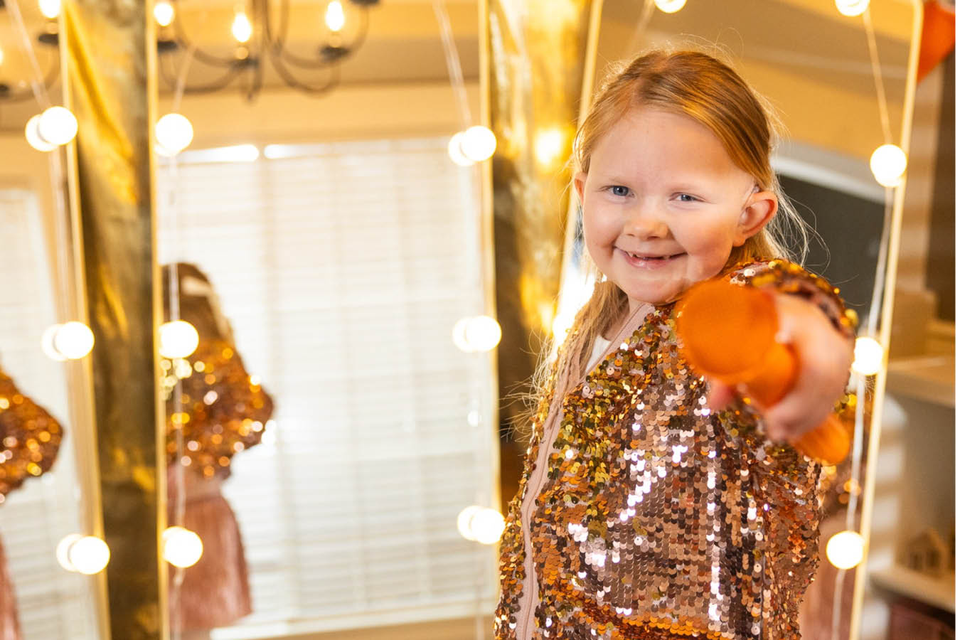 A girl in sparkly clothes points a microphone at the camera