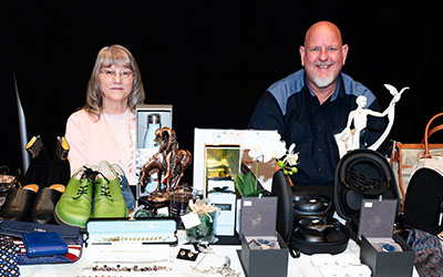 A woman and a man sit a table with an assortment of thrift items