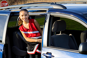 A school-aged girl wearing a red, white and black cheerleading uniform climbs into the backseat of a blue vehicle