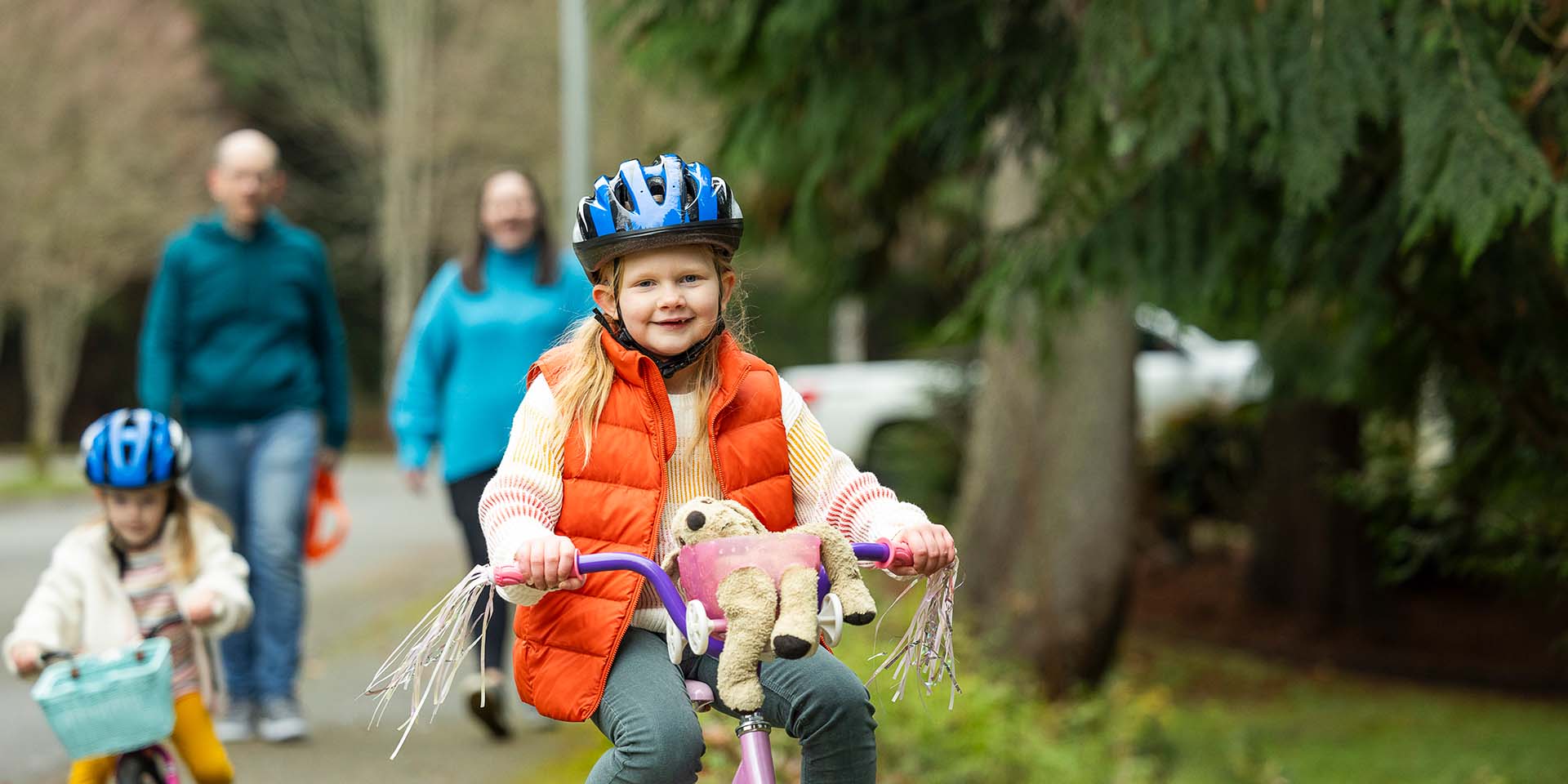 A girl wearing a helmet rides a bike in front of her family