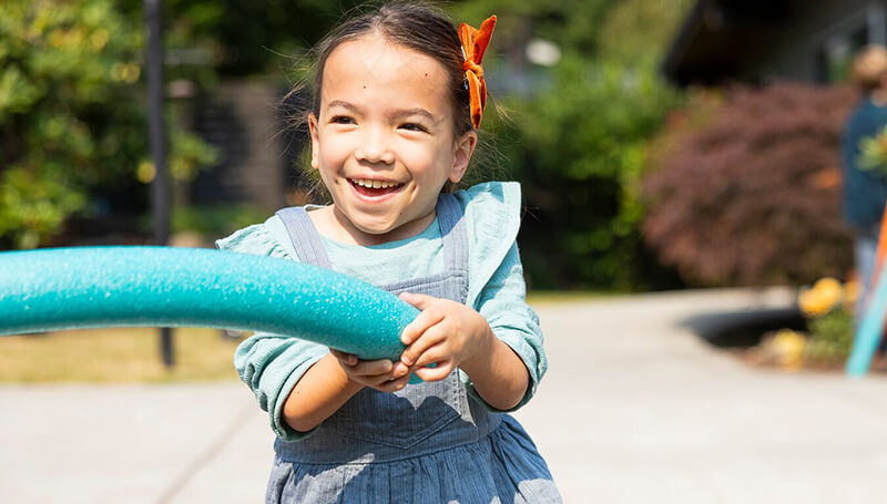 A girl happily playing with a pool noodle toy