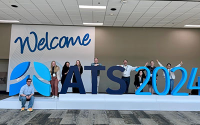 Residents stand on a sign that reads Welcome ATS 2024