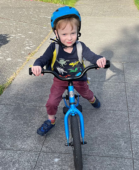 A 5-year-old rides a balance bike on a sidewalk with an immunotherapy study drug in his backpack.