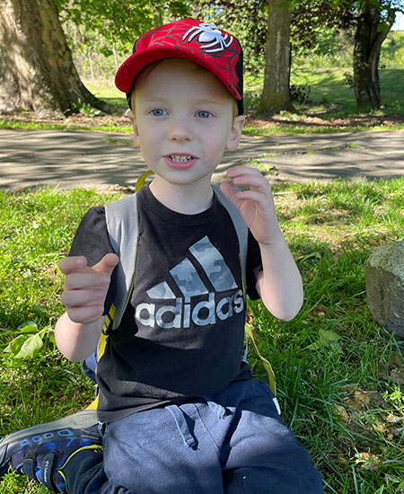 A boy with a backpack sits in a forest clearing