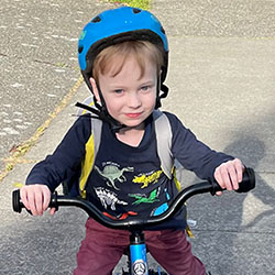 A 5-year-old boy rides a balance bike on a sidewalk with an immunotherapy study drug in his backpack. 